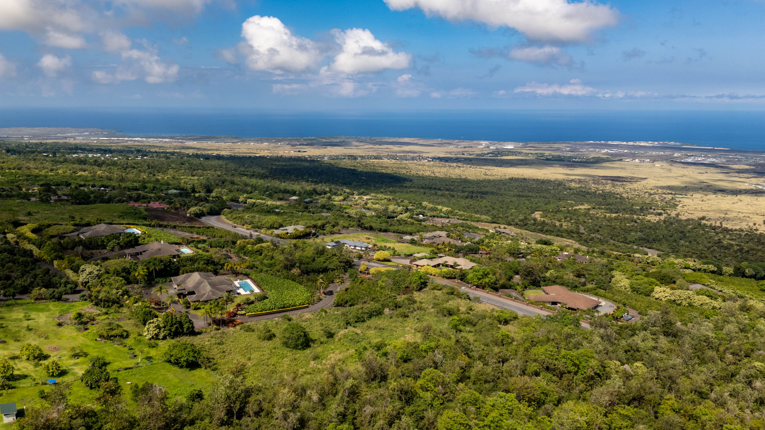 Aerial view of luxury homes in Kona, Hawaii, showcasing lush greenery, ocean views, and the elevation of the landscape, highlighting the appeal of upscale living and real estate opportunities in the region.