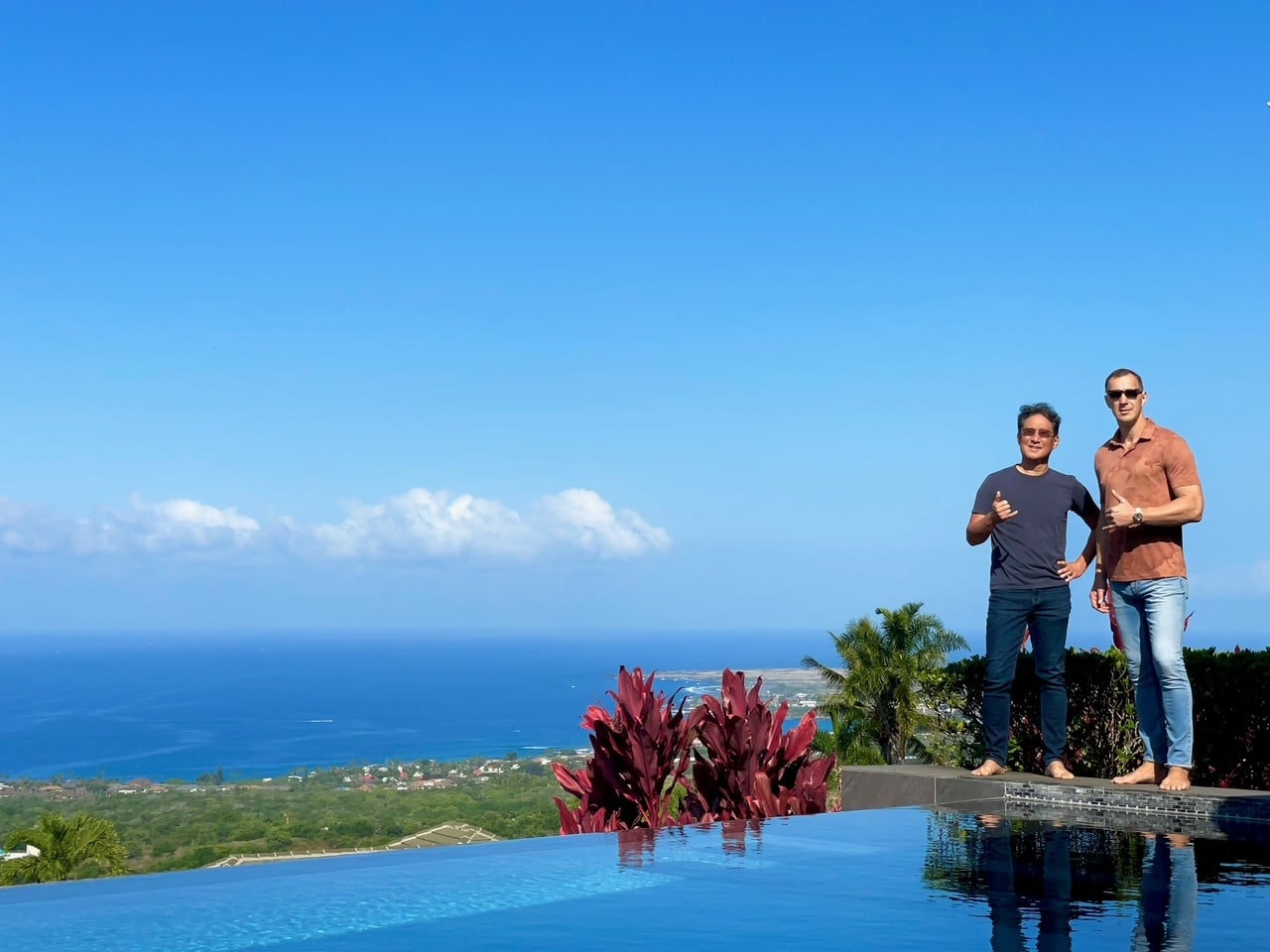 Two men standing by a swimming pool with ocean view in Kailua-Kona, Hawaii, showcasing the luxury real estate market.