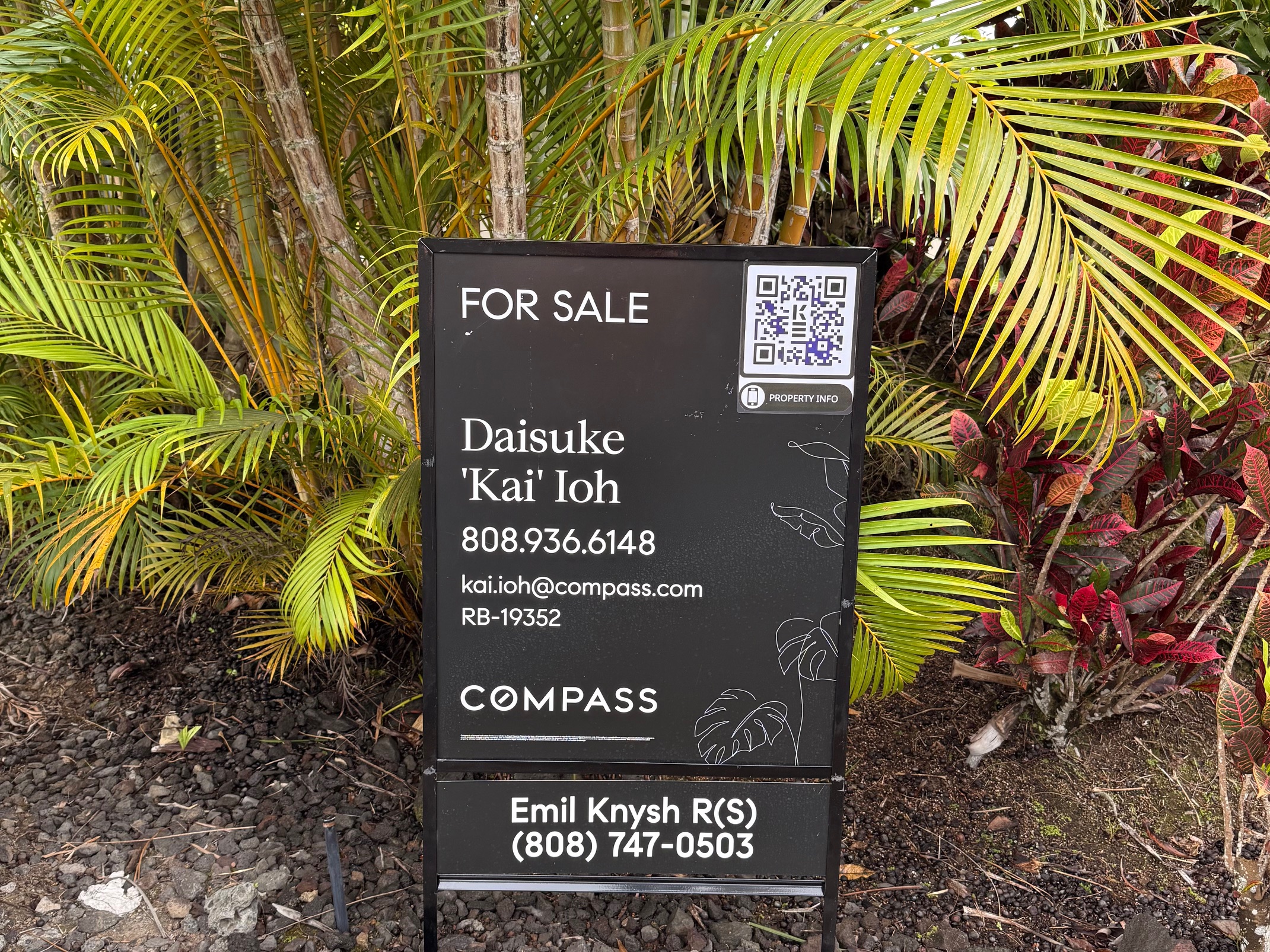 For sale sign featuring Daisuke 'Kai' Ioh's contact information and QR code, surrounded by tropical foliage, promoting real estate services in Kailua-Kona, Hawaii.